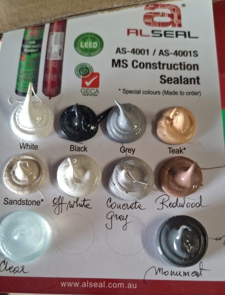 A collection of color samples displayed on a piece of paper, featuring various shades such as white, black, grey, teak, sandstone, off-white, concrete, monument and redwood. The background includes branding and information related to ALSEAL MS Construction Sealant.